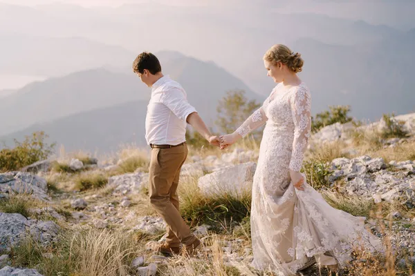 Novia y novio caminan por la montaña tomados de la mano —  Fotos de Stock