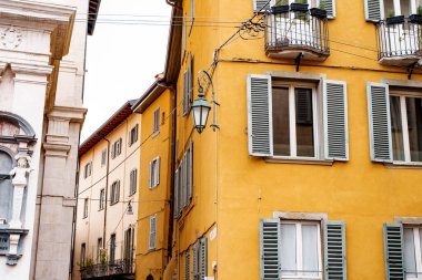 Pencereleri panjurlu eski bir evin köşesindeki metal fener. Bergamo, İtalya