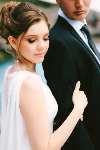 Noiva com penteado alto em um vestido branco segura o braço do noivo em uma jaqueta preta e camisa branca. Fechar — Fotografia de Stock