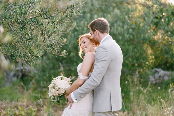 Damat gelini zeytin ağacının yanında bir buket çiçekle kucaklıyor. — Stok fotoğraf