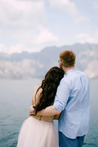 Les mariés s'embrassent sur la jetée dans la baie de Kotor, vue de dos — Photo