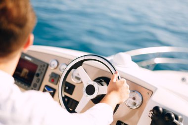 Beyaz gömlekli bir adam beyaz bir motorlu tekne kullanıyor. Yakın plan.
