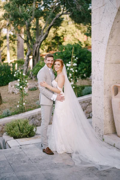 Vőlegény ölelés menyasszony közel kő fal zöld parkban — Stock Fotó