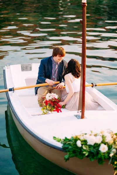Mosolygó férfi és nő egy csokor virággal lovagolnak egy csónakban a vízen — Stock Fotó