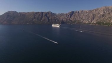 Yolcu gemisi bir dağ sırasını geçerek deniz körfezi boyunca yelken açar.