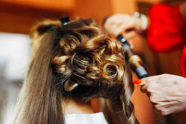 Hairdresser makes bride a high wedding styling with curls with a curling iron. Close-up — Stock Photo, Image