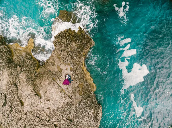 Homem e mulher deitam-se abraçando nas rochas pelo mar azul espumante. Vista de cima — Fotografia de Stock