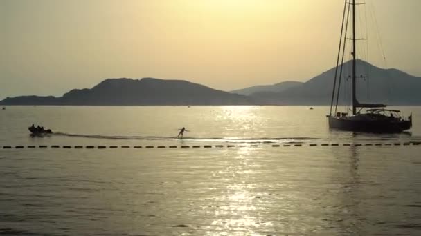 Man rides a jet ski on the sea against the backdrop of a sailboat at sunset — Stock Video