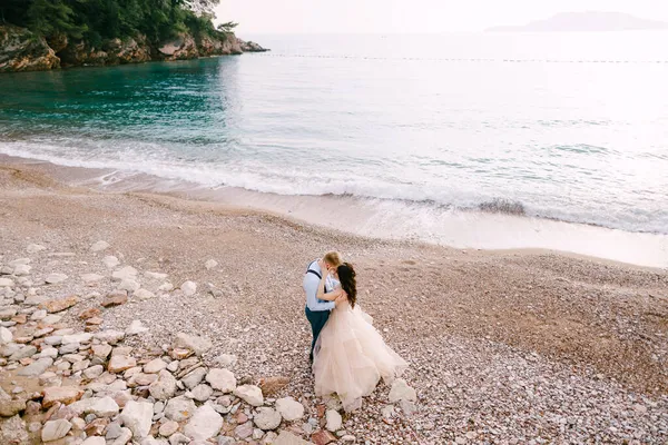 Braut und Bräutigam stehen am Kiesstrand und umarmen sich — Stockfoto