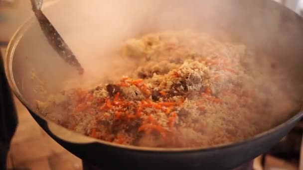 Cook mixes rice with meat and carrots with a slotted spoon in a cauldron — Stock Video