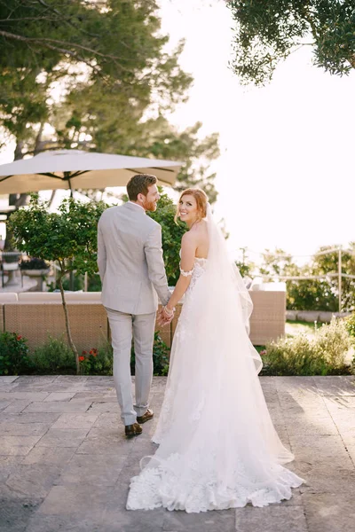 Νύφη και γαμπρός κρατήστε τα χέρια, ενώ στέκεται κοντά στις πολυθρόνες κάτω από μια ομπρέλα από τον ήλιο — Φωτογραφία Αρχείου