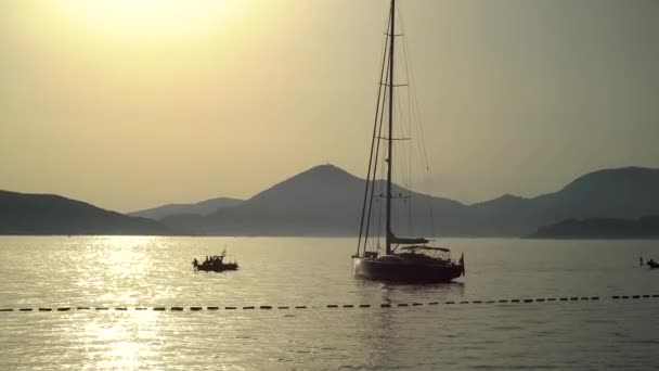 喜びのボートは山を背景に日没時に海の中の帆船を通り過ぎます — ストック動画