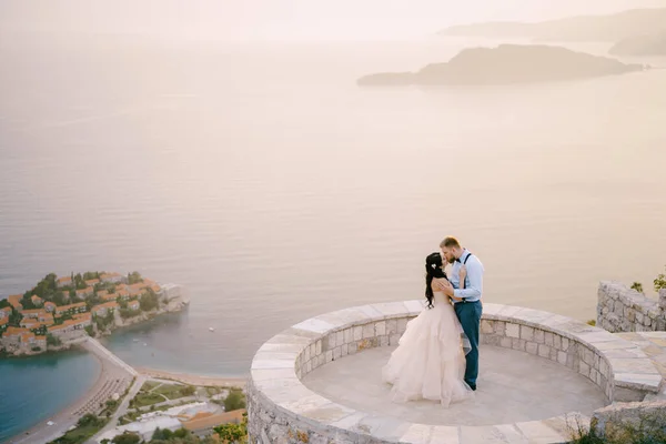 Panna młoda i pan młody ściskają się na tarasie widokowym z widokiem na wyspę Sveti Stefan — Zdjęcie stockowe