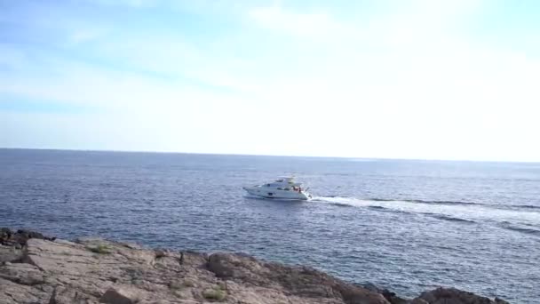 モーターヨットは岩の多い海岸を越えて海を航海します — ストック動画