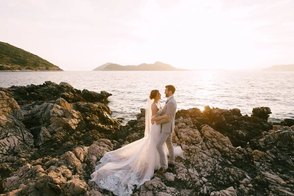 Brudgum och brud står kramas varandra på klipporna vid havet — Stockfoto