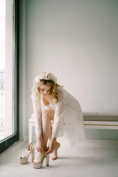 Νύφη σε λευκό δαντέλα peignoir φοράει ψηλά τακούνια σανδάλια κατά την προετοιμασία για την τελετή του γάμου — Φωτογραφία Αρχείου