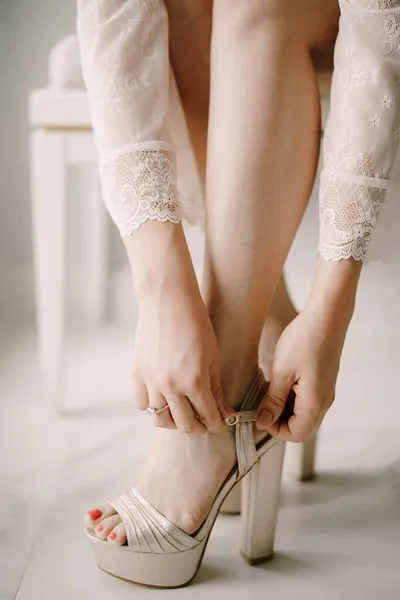 Bruid in wit kant peignoir draagt hoge hakken sandalen ter voorbereiding op de bruiloft ceremonie, close-up — Stockfoto