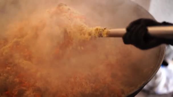 Chef mezcla el pilaf uzbeko con una cuchara ranurada en un caldero — Vídeos de Stock