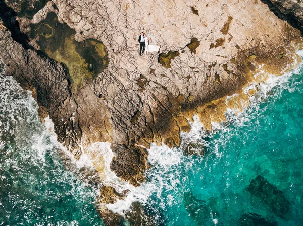 Os recém-casados encontram-se abraçados na costa rochosa perto do mar. Vista aérea — Fotografia de Stock