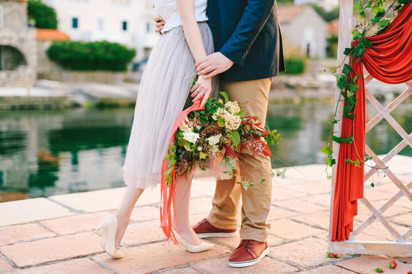 Man knuffelt vrouw met een boeket bloemen in haar handen terwijl ze op de pier staat in de buurt van een decoratief scherm tegen de achtergrond van oude huizen — Stockfoto