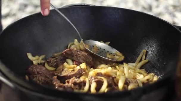 Agitar la carne y la cebolla guisando en un caldero con una cuchara ranurada — Vídeo de stock