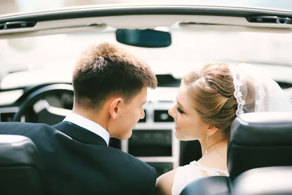 Frischvermählte lächeln einander an, während sie in einem Cabrio sitzen. Nahaufnahme — Stockfoto