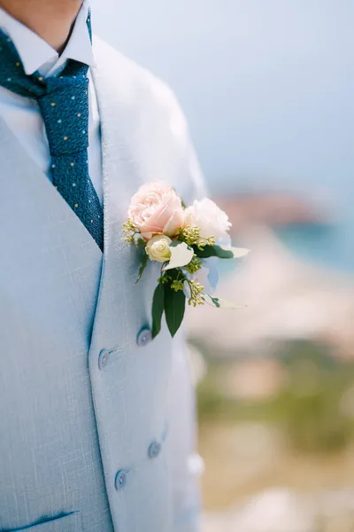 Ένας άντρας με μπλε γιλέκο, μπλε γραβάτα και ένα ντελικάτο μπουτονιέρα με τριαντάφυλλα και ευκάλυπτο, κοντινό πλάνο. — Φωτογραφία Αρχείου