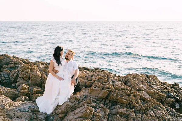 La novia se sienta en las rodillas del novio en la costa rocosa —  Fotos de Stock
