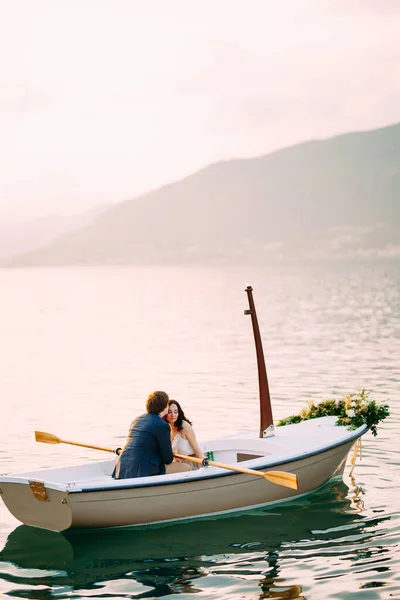 Homem beija mulher na testa em um barco decorado com flores no meio de uma lagoa contra um fundo de montanhas — Fotografia de Stock