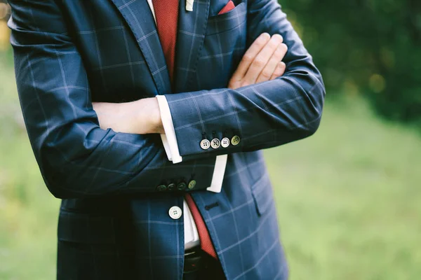 El novio con un traje a cuadros azul, camisa blanca y corbata roja está de pie con los brazos cruzados sobre su pecho. Primer plano —  Fotos de Stock