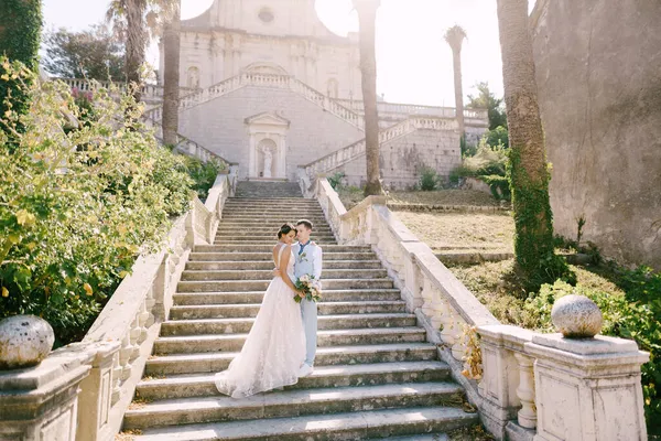 Bruden och brudgummen står kramas på trappan till Födelsekyrkan av Jungfru Maria kyrka i Prcanj — Stockfoto