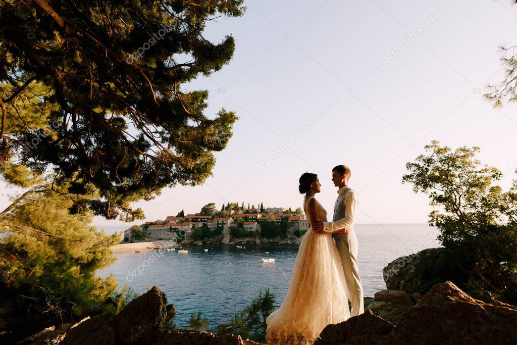 Bride and groom embrace against the backdrop of the island of Sveti Stefan. Montenegro