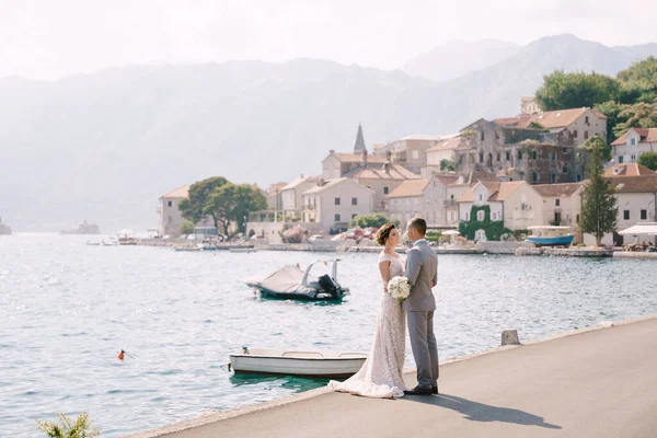 Bräutigam und Braut stehen auf dem Pier am Meer vor dem Hintergrund von Gebäuden — Stockfoto