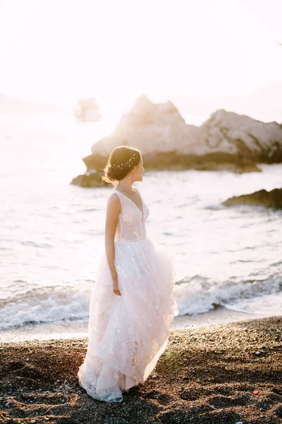 Nevěsta v bílých vyšívaných šatech stojí na písčitém břehu. Černá — Stock fotografie