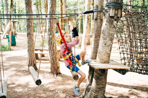 Chłopiec w pasach bezpieczeństwa wspina się na platformę drzew przez most zwinności — Zdjęcie stockowe