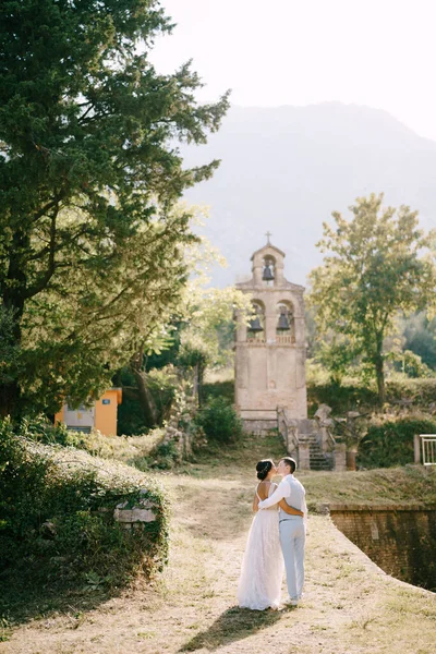 Noiva e noivo abraçando e beijando perto da antiga torre sineira perto da igreja em Prcanj, vista para trás — Fotografia de Stock