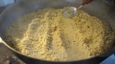 Şef pilavla pilavı bir kaşıkla kazanda karıştırıyor.
