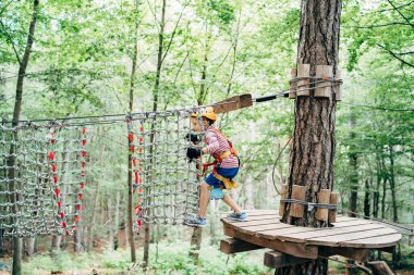 Çocuk ahşap bir platformdan ağ köprüsüne adım atıyor.