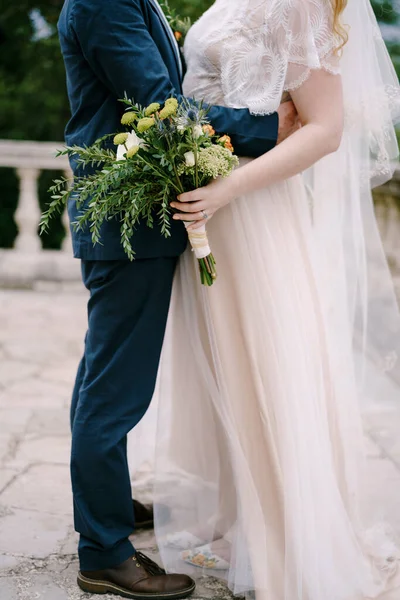 Жених обнимает невесту с букетом на каменной террасе — стоковое фото
