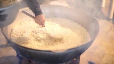 Aşçı Özbek pilavı pişirmek için bir kâseden bir kazana pirinç döker