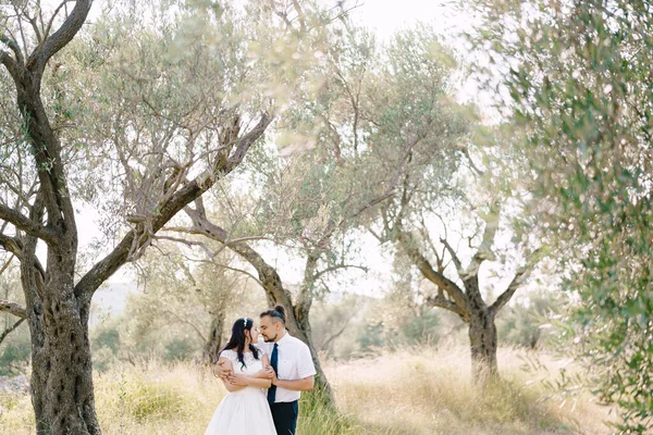 Жених обнимает невесту, стоя между деревьями в зеленом парке — стоковое фото