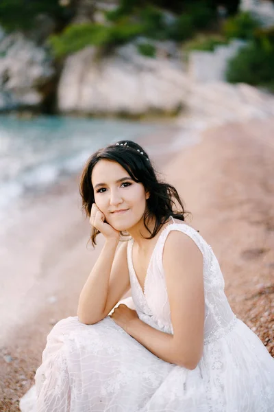 Tersenyum pengantin dalam gaun putih duduk di pantai — Stok Foto