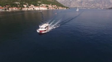 Turist teknesi arka planda dağlarla birlikte Kotor Körfezi boyunca yol alır. Karadağ