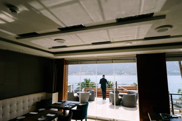 Ο άνθρωπος στέκεται στο μπαλκόνι ενός πολυτελούς ξενοδοχείου και έχει θέα στη θάλασσα. Πίσω όψη — Φωτογραφία Αρχείου