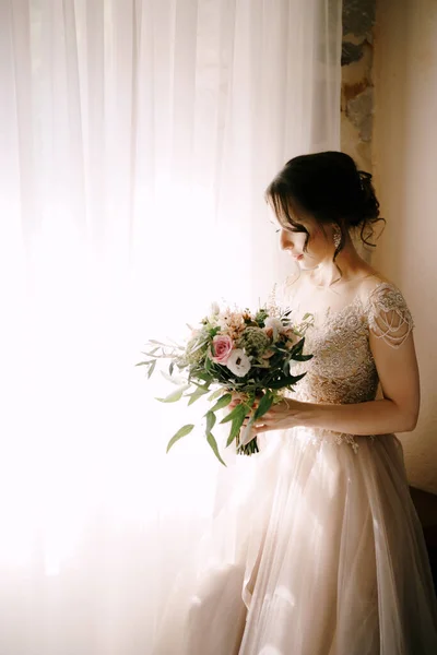 Noiva em um vestido de renda olha para um buquê de flores em suas mãos — Fotografia de Stock