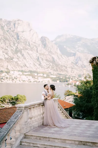 Vőlegény ölelés menyasszony közel a korláton a háttérben a hegyek — Stock Fotó