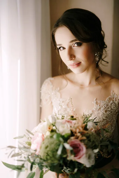 Porträtt av bruden i en klänning med en bukett blommor vid fönstret — Stockfoto