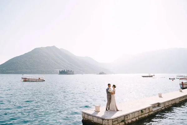 Bräutigam umarmt Braut an einem sonnigen Tag auf der Seebrücke am Meer — Stockfoto