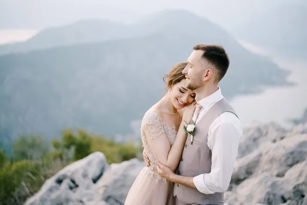 O noivo sorridente abraça a noiva na montanha. Retrato — Fotografia de Stock