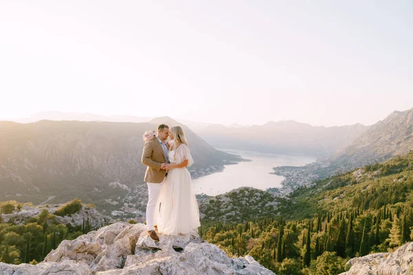 Νύφη και γαμπρός στέκονται σε ένα βραχώδες βουνό με θέα στον κόλπο — Φωτογραφία Αρχείου